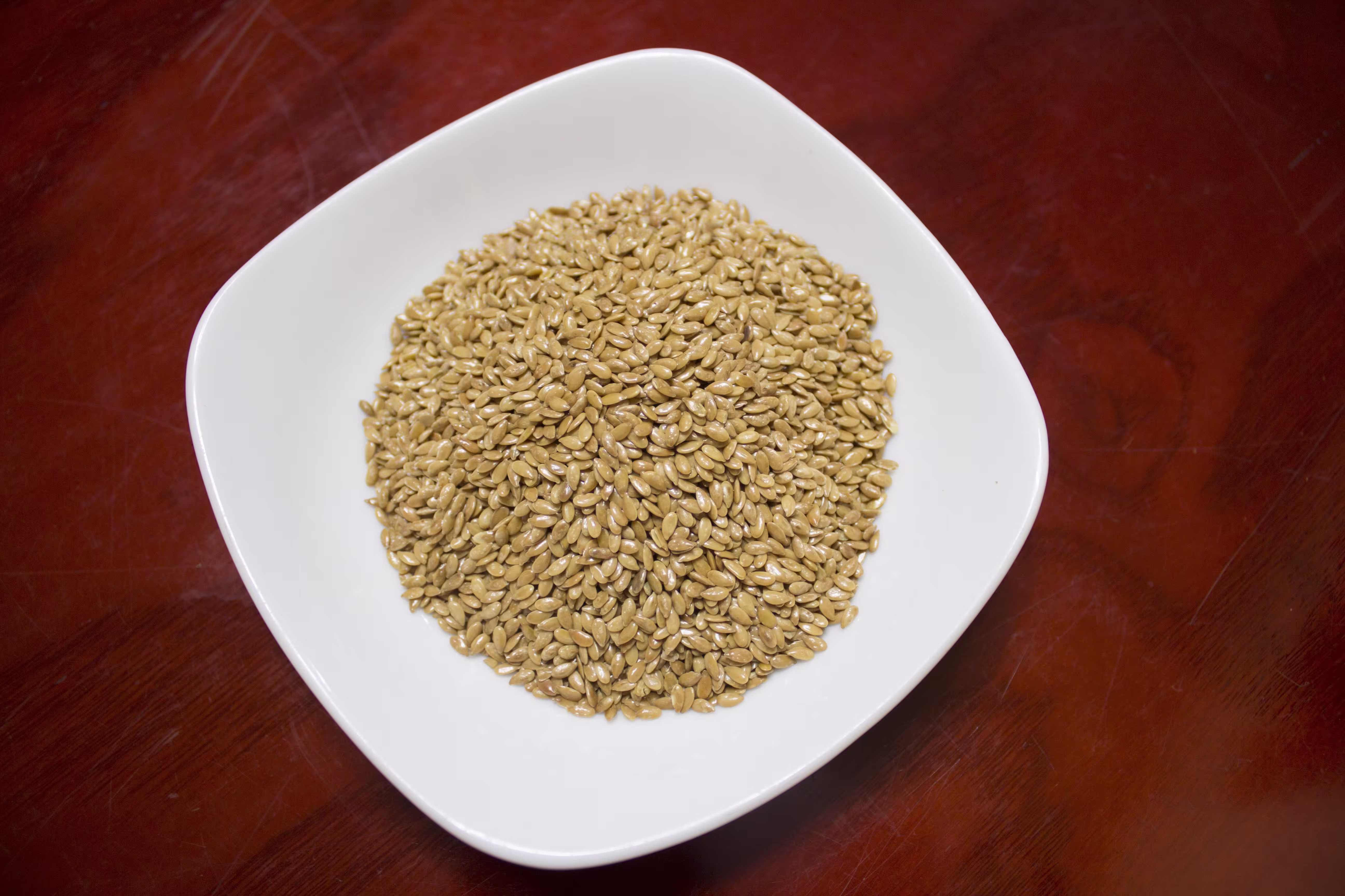 ajwain seed in white bowl on a wooden table, showing their natural brown color in light.